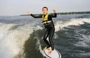 A Woman in a Yellow Life Vest and Black Wetsuit Rides a Wakesurf