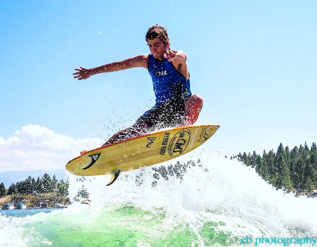 A Male Wakesurfer Wearing a Blue Tank Top Performs an Aerial Trick Above the Water